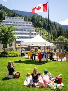 A band plays in a park with a Canadian flag and large mine building in the background 