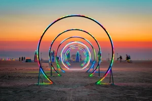 Watchful Eye Mathias Horne A series of lit circles in placed in the desert with the sun setting behind