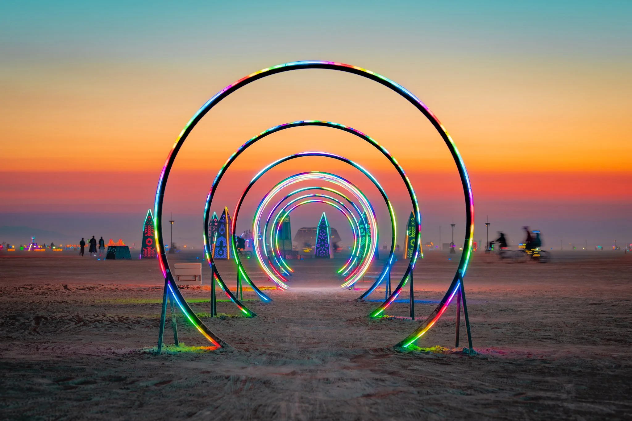 A series of lit circles in placed in the desert with the sun setting behind